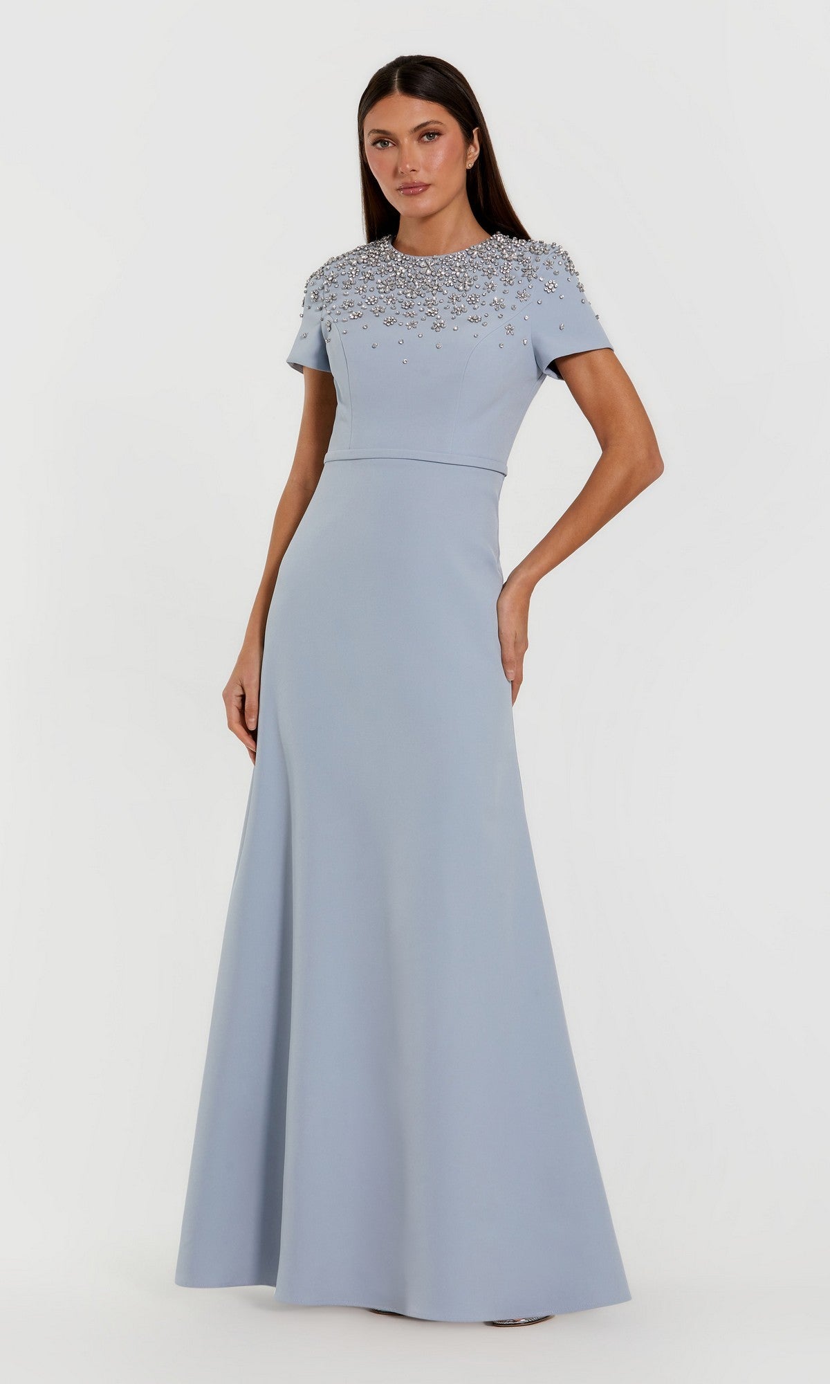 A woman wearing the Mac Duggal 50038 long formal dress in powder blue—a floor-length crepe trumpet gown adorned with bead embellishments on the bodice and featuring short sleeves—standing against a plain white background.